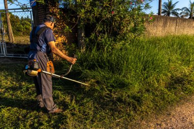 Marilia, Sao Paulo, Brezilya, 22 Mart 2023. İşçi, manuel benzin fırça kesicisiyle Marilia 'nın kırsal kesimindeki bir çiftliğin kapısındaki yağmurla birlikte büyüyen otları kesiyor.
