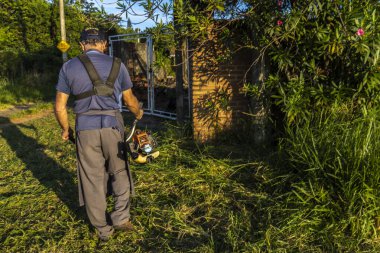 Marilia, Sao Paulo, Brezilya, 22 Mart 2023. İşçi, manuel benzin fırça kesicisiyle Marilia 'nın kırsal kesimindeki bir çiftliğin kapısındaki yağmurla birlikte büyüyen otları kesiyor.