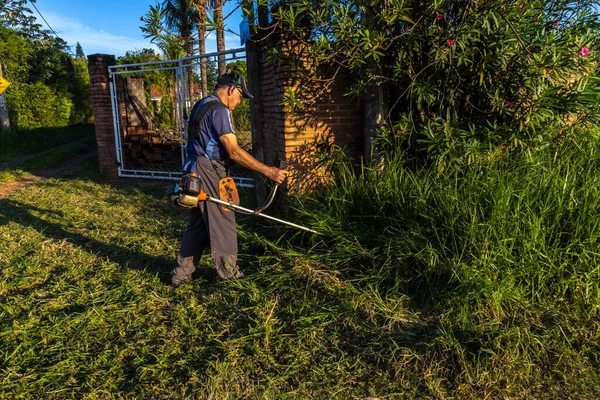 stock image Marilia, Sao Paulo, Brazil, March 22, 2023. Worker, with a manual gasoline brush cutter, cuts the weeds that grew with the rains in front of the gate of a farm in the rural area of Marilia, SP