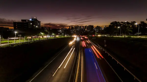 Trail of light caused by vehicular traffic in Highway with buildings from downtown in the background, in Marilia