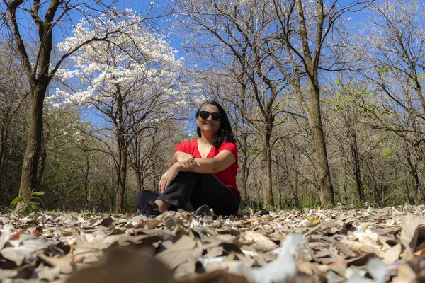 Brezilya 'da beyaz bir sarmaşık ormanında (Tabebuia roseo-alba) yerde oturan orta yaşlı kadın..