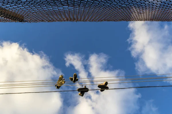 Wire mesh fence and old shoes hanging on electrical wire against a sky in Brazil. Shoe tossing