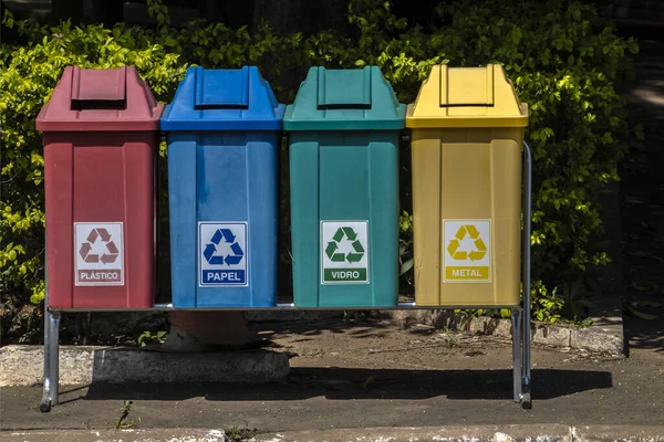 Four color trash cans for recycling, with the words Plastic, Paper, Glass and Metal in Portuguese on the park in Brazil