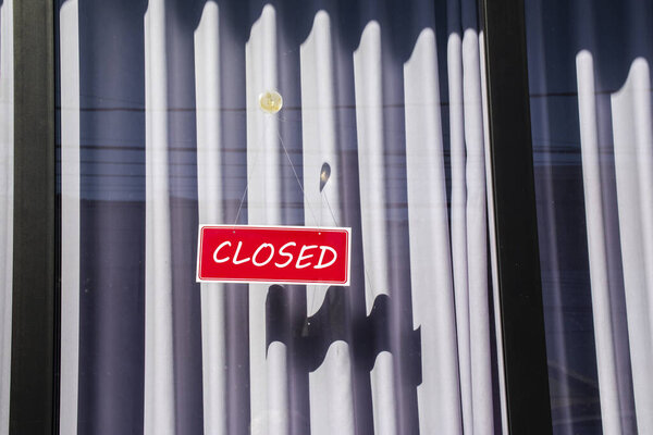 Знак со словом closed на стеклянной двери с закрытой занавеской магазина, расположенного в Бразилии