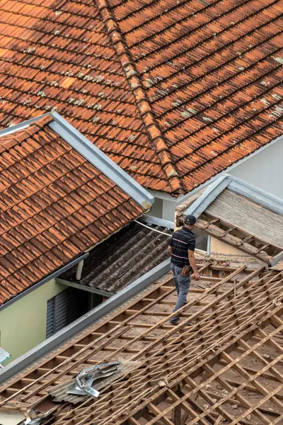 stock image Marilia, Sao Paulo, Brazil, August 29, 2023. Top view of a worker removing tiles from a house to renovate the roof of a commercial point in the city center of Marilia