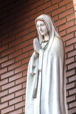 Katolik dininde Tanrı 'nın annesi Fatima' nın heykeli, Fatima 'nın Hanımı, Brezilya' daki tuğla duvarın arka planında Bakire Meryem 'in heykeli.