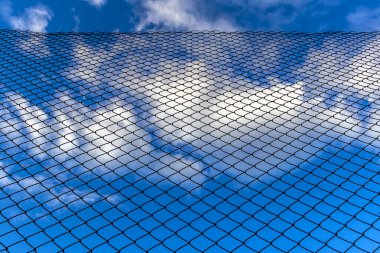 Bulutlu mavi bir gökyüzünde alçak açılı çit bulutlu ağ çiti bulutlu gökyüzü, zincirli tel örgüler mavi gökyüzü, çit ve Brezilya 'nın ötesindeki mavi gökyüzü.