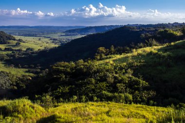 Ormanı, nehri, okaliptüs ağaçları ve çayırları olan güneşli yeşil dağ vadisinin renkli manzarası. Brezilya 'da bulutlu gökyüzünün altındaki sıradağlara karşı. Gün ışığında geniş dağ vadisi.