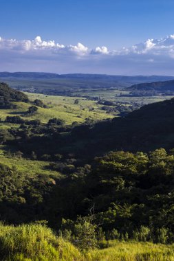 Ormanı, nehri, okaliptüs ağaçları ve çayırları olan güneşli yeşil dağ vadisinin renkli manzarası. Brezilya 'da bulutlu gökyüzünün altındaki sıradağlara karşı. Gün ışığında geniş dağ vadisi.