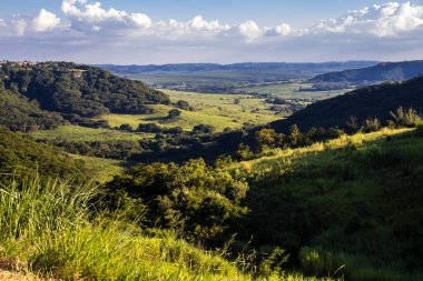 Ormanı, nehri, okaliptüs ağaçları ve çayırları olan güneşli yeşil dağ vadisinin renkli manzarası. Brezilya 'da bulutlu gökyüzünün altındaki sıradağlara karşı. Gün ışığında geniş dağ vadisi.