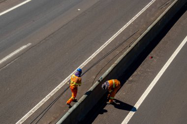 Marilia, SP, Brazil, March 12, 2024. Construction workers install guardrails to prevent people from passing through the concrete median of a highway in Brazil. This will reduce collisions. clipart