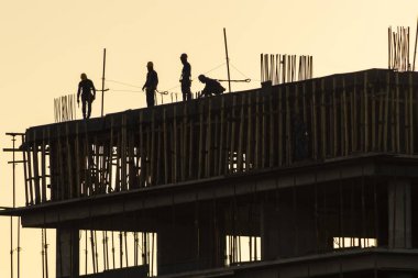 İnşaat alanı, gün batımına karşı iskelede çalışan inşaat işçilerinin siluetleri. Brezilya 'da inşaat ve inşaat endüstrisi