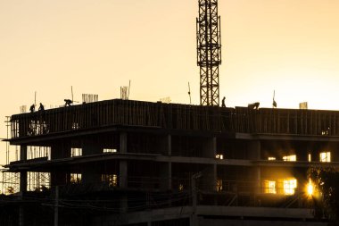 İnşaat alanı, gün batımına karşı iskelede çalışan inşaat işçilerinin siluetleri. Brezilya 'da inşaat ve inşaat endüstrisi