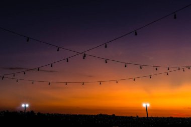 Brezilya 'da günbatımı arkaplanlı kablolarda asılı duran sıra sıra ampul lambaları silueti