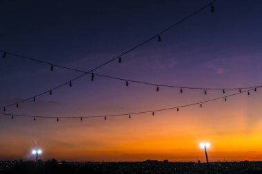 Brezilya 'da günbatımı arkaplanlı kablolarda asılı duran sıra sıra ampul lambaları silueti