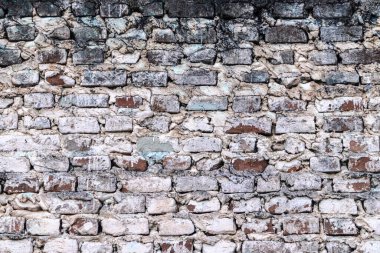 Yıpranmış dokusu olan eski tuğla bir duvar. Tuğlalar, gri ve beyaz tonlarında, yaşlanma ve maruz kalma belirtileri gösteriyor..