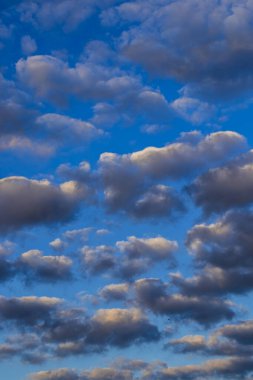 Yoğun ve şehvetli bulutlarla dolu canlı, mavi bir gökyüzü. Dramatik ışıklandırma bulutların dokusunu vurgular, aydınlık ve karanlık tonlarda farklılık gösterir, çekici bir görsel karşıtlık yaratır..