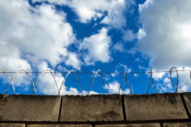 Mavi gökyüzüne karşı dikenli telle kaplı beton duvar. Güvenlik, sınırlar, özgürlük ve doğal ve inşa edilmiş konuları gözler önüne serer..