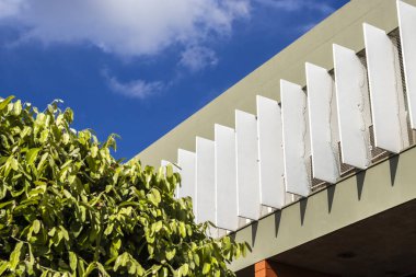 Doğa ve mimari arasındaki etkileşimi gösteren resimler. Gri tuğla duvarlar, yemyeşil alanlar, palmiye ağaçları ve modern bina detayları. Kentsel tasarım ve sürdürülebilirliği göstermek için ideal