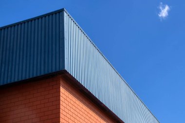 Tuğla tabanlı ve mavi metal kaplamalı bir binanın köşesi, malzeme ve çağdaş mimaride karşıtlık sergiliyor.