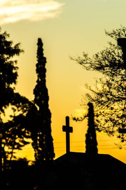Mezarlık siluetleri alacakaranlıkta, renkli gökyüzüne karşı haçlar ve heykellerle. İnanç, hafıza ve yansıma temalarını çağrıştırır