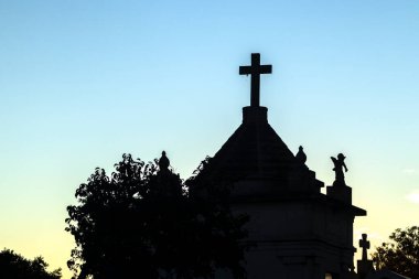Mezarlık siluetleri alacakaranlıkta, renkli gökyüzüne karşı haçlar ve heykellerle. İnanç, hafıza ve yansıma temalarını çağrıştırır