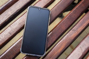 Ahşap bir bankta akıllı telefon. Günlük yaşamda teknoloji, dijital iletişim ve mobil cihaz kullanımı.