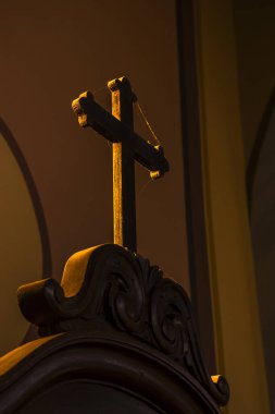 Brezilya 'da bir Katolik kilisesinde loş ışıkta yıkanan ahşap haç ve karmaşık detaylar. İnancı, tarihi ve kültürü çağrıştırıyor. Dini, tarihi veya sanat temaları için ideal.