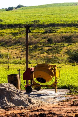 Kırsal bir ortamda kum yığınıyla birlikte sarı beton karıştırıcı. Brezilya 'da inşaat işi, altyapı ve kırsal yaşamı resmediyor.