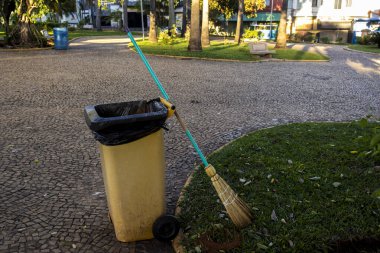 Brezilya şehrinin bir meydanında saman süpürgesiyle gezici sarı çöp kutusu. Kentsel temizlik ve atık yönetimi.