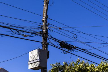 Tangled wires on a wooden utility pole against a clear blue sky. Illustrates urban infrastructure and power distribution challenges in Brazil.