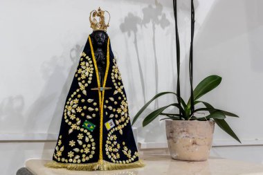 Image of Our Lady Aparecida, patron saint of Brazil, with a black mantle, gold details and flags.