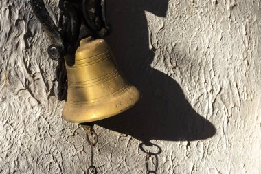 Golden bell casting a dramatic shadow on a textured wall in Brazil. Side lighting enhances the bell shaped and walls texture.