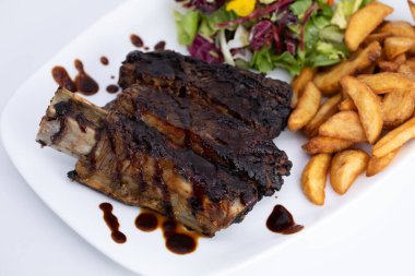 Beyaz tabakta, patates kızartması ve salata ile nefis sığır pirzolası.