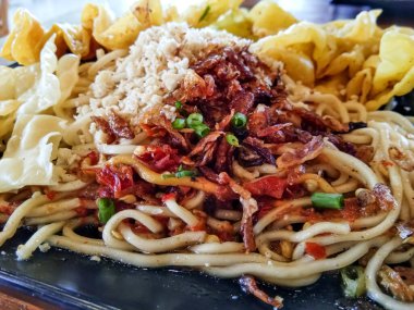 close up spicy noodles topped with shredded chicken and chicken dumplings as a complement