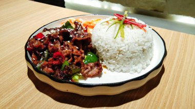 Teriyaki tavuğu, pirinçli ve dilimlenmiş havuç. Tahta bir masada beyaz bir tabakta.