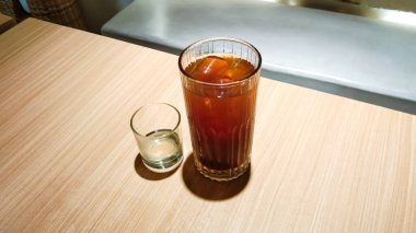 Bir bardak buzlu çay, küçük bir bardakta, ahşap bir masada sıvı şeker.