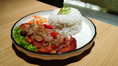Tahta bir masada sambal matah ve taze sebzeli bir tabak pirinç ve tavuk katsu.