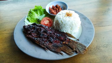 Ahşap bir masada, marul ve domatesli ızgara gurami salatası ve biber sosu.