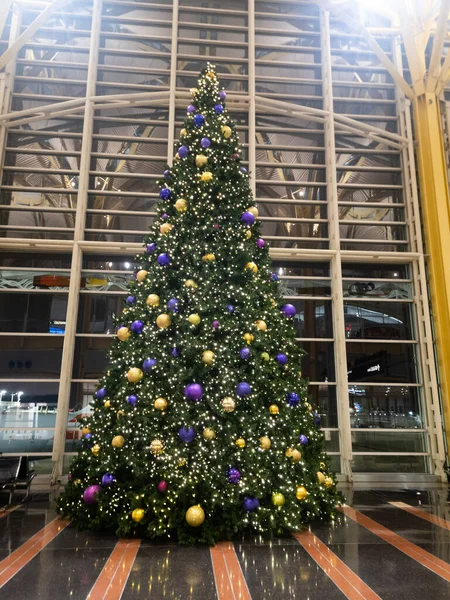 Christmas Tree at Ronald Reagan Washington National Airport, terminal 2 at night. The tree has gold and purple Christmas ornaments.