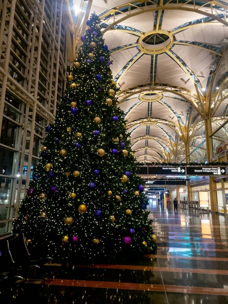Christmas Tree at Ronald Reagan Washington National Airport, terminal 2 at night. The tree has gold and purple Christmas ornaments.