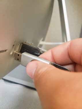 Metal bir USB flaş belleği tutan ve USB yuvasında bir Apple bilgisayarının arkasına yerleştiren bir el.