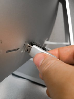 Metal bir USB flaş belleği tutan ve USB yuvasında bir Apple bilgisayarının arkasına yerleştiren bir el.