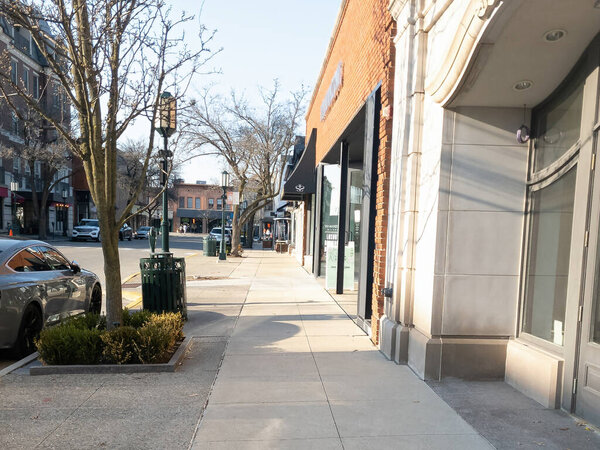 A view from the sidewalk in downtown Birmingham, Michigan in early April with a brick building in front and trees