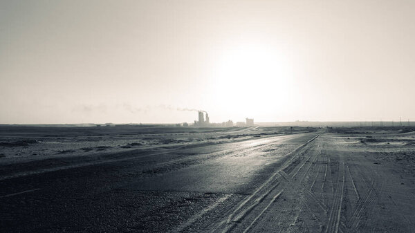 Silhouette of the cement factory in the middle of the desert and the smoke rising high and stretching long away from it-