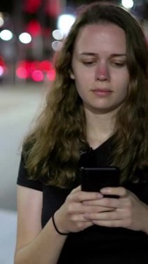 Geceleri sokakta yürürken cep telefonuyla mesajlaşan genç bir kadın - seyahat fotoğrafçılığı