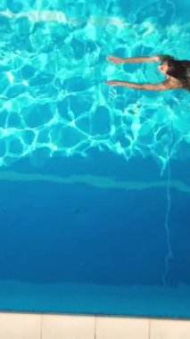 Young woman enjoys swimming in the cool water of a pool in summertime - view from above - Vertical video