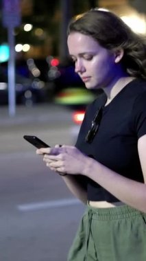 Geceleri sokakta yürürken telefonuyla mesajlaşan genç bir kadın. Seyahat fotoğrafçılığı.