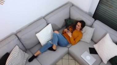 Kanepede sörf yaparken dinlenen güzel bir kız telefon görüşmesi yapıyor.