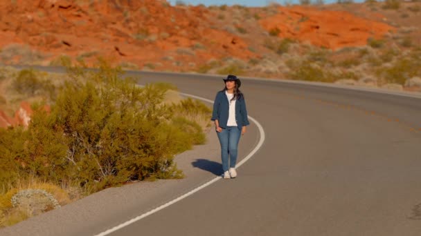 カウボーイの帽子をかぶった若い女性は アリゾナの砂漠の石灰色の道を歩いています 旅行写真 — ストック動画